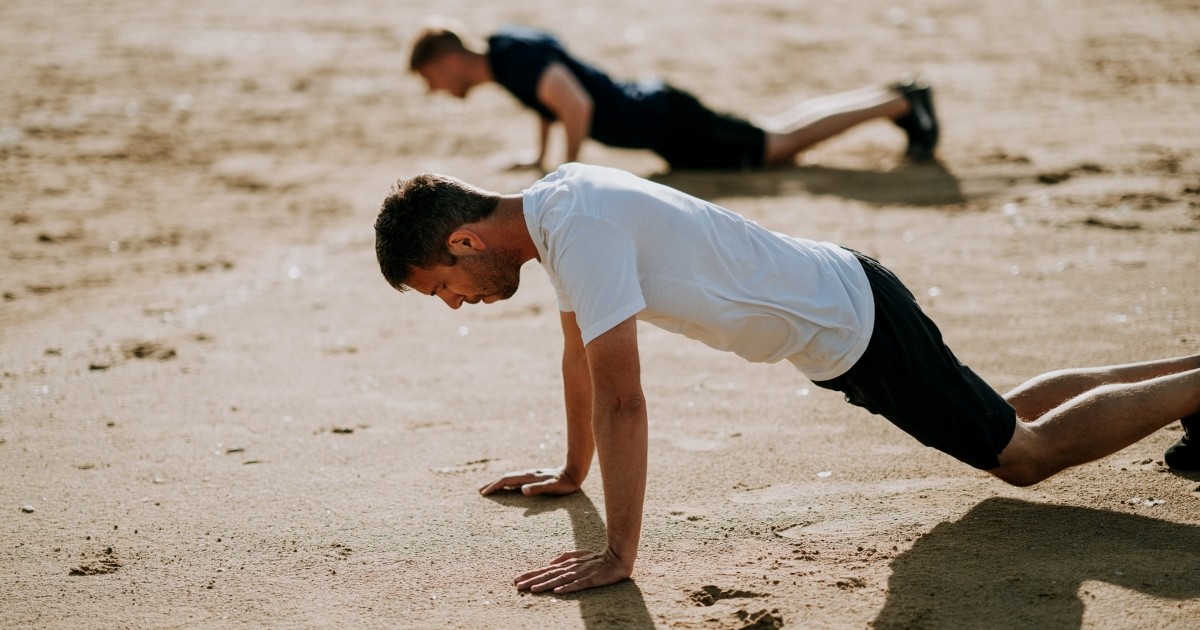 Two men doing planks or pushups on a beach. Photo by Annie Spratt via Unsplash.